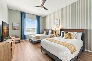 Une chambre d’hôtel avec deux lits, un ventilateur de plafond, une fenêtre avec des rideaux, un bureau avec une chaise et une plante.