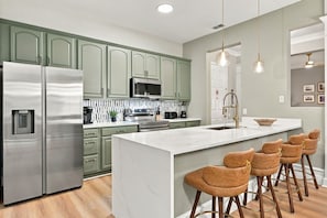 A modern kitchen with stainless steel appliances, green cabinets, and a marble island with bar stools. - Vista Cay 3BR Condo, Lake View, Near Universal (Orlando)