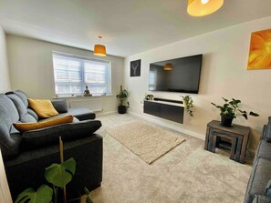 Ein modernes Wohnzimmer mit einem grauen Sofa, einem Flachbildfernseher und einem kleinen Beistelltisch mit einer Pflanze.