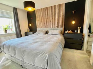 A bedroom with a bed, bedside tables, a dresser, a lamp, and a window with curtains. - Modern 3Bed House • Parking • WiFi • Hampton Water (Peterborough)