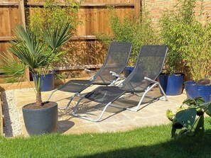 Two lounge chairs with metal frames and mesh seats, positioned on a patio with a potted plant and a wooden fence in the background. - Modern 3Bed House • Parking • WiFi • Hampton Water (Peterborough)