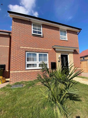 A two-story brick house with a front door, two windows with shutters, and a small porch. - Modern 3Bed House • Parking • WiFi • Hampton Water (Peterborough)