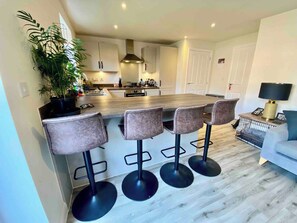 A modern kitchen with a central island, bar stools, and a dining area. - Modern 3Bed House • Parking • WiFi • Hampton Water (Peterborough)