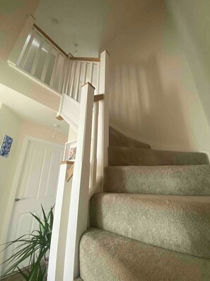 Eine Treppe mit Handlauf und Teppichstufen, die zu einer oberen Etage führt.