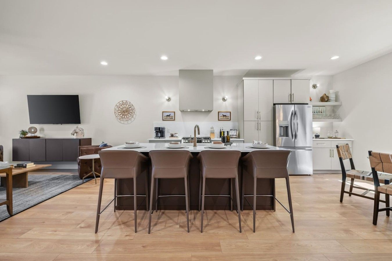 A modern kitchen with a dining area, featuring a central island, white cabinetry, and stainless steel appliances.