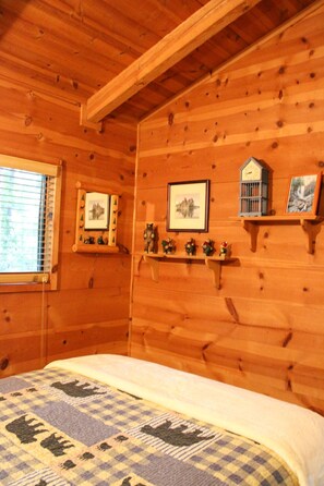 Ein Schlafzimmer einer Holzhütte mit einem Bett, einem Fenster mit Jalousien und Wandregalen mit dekorativen Gegenständen.
