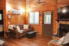 A cozy cabin interior with a wooden floor, a sofa, a fireplace, and a television. - 47 Bear Ridge cozy 2 bedroom 1 bathroom cabin. Perfect getaway (Sautee)