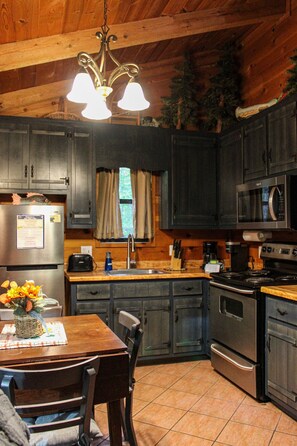 A kitchen with wooden cabinets, a stainless steel refrigerator, a microwave, a stove, and a dining table with chairs. - 47 Bear Ridge cozy 2 bedroom 1 bathroom cabin. Perfect getaway (Sautee)