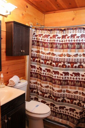 A bathroom with a wooden cabin interior, a toilet, a sink, and a shower curtain with animal patterns. - 47 Bear Ridge cozy 2 bedroom 1 bathroom cabin. Perfect getaway (Sautee)