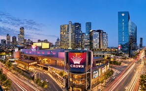 Une vue urbaine mettant en scène un hôtel imposant, reconnaissable à son grand panneau lumineux, et entouré d’immeubles modernes de grande hauteur.