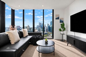 A modern living room with a black leather sofa, a round coffee table, and a large TV on the wall. - Skyline Noir City Views near Melbourne Highlights (Melbourne)