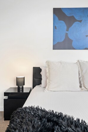 A bedroom with a bed, a nightstand, a lamp, a painting, and a black furry rug. - Skyline Noir City Views near Melbourne Highlights (Melbourne)