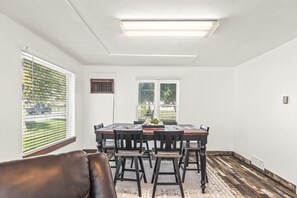Un comedor con una mesa y sillas, una ventana con persianas, una lámpara en el techo y una alfombra estampada.