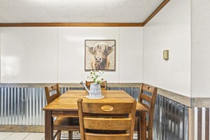 Ein Essbereich mit einem Holztisch und Stühlen, einer Blumenvase und einem Bild einer Kuh an der Wand.