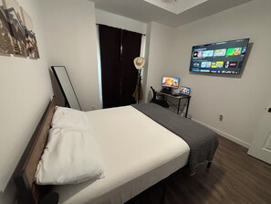 A hotel room with a bed, a desk with a computer, and a TV displaying movie options. - Private Room in Brandnew Home. Fullsize Bathroom & Kitchen. 5min from Airport (Harlingen)