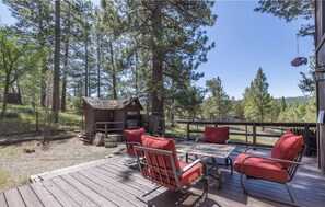 A wooden deck with outdoor furniture, a small cabin, and a forested backdrop. - Family game room, great views, & steps to marina! (Big Bear Lake)