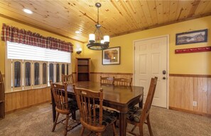 A dining room with a wooden table and chairs, a chandelier, a window with blinds, and a door. - Family game room, great views, & steps to marina! (Big Bear Lake)