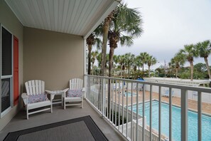 A balcony with two white Adirondack chairs, a pool, and palm trees in the background. - Beachside Escape at the Gulfplace with Pools, Hot Tubs and Fine/Casual Dinning (Santa Rosa Beach)
