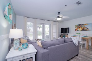 A living room with a grey sofa, a white coffee table, a TV, and a dining area with a wooden table and chairs. - Beachside Escape at the Gulfplace with Pools, Hot Tubs and Fine/Casual Dinning (Santa Rosa Beach)