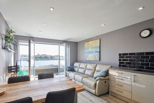 A modern living room with a sofa, a dining table, and a kitchen area.