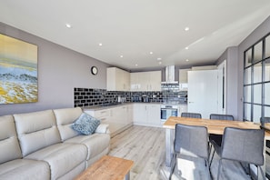 A modern kitchen with white cabinets, a black backsplash, and a dining area with a wooden table and chairs. - Host Stay Fish Quay View (North Shields)