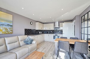 A modern kitchen with white cabinets, a black backsplash, and a dining area with a wooden table and chairs.