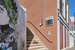 A brick building with a staircase leading to an upper level, a sign indicating 'WATERFRONT APARTMENTS 1-4', and a CCTV security camera. - Host Stay Fish Quay View (North Shields)
