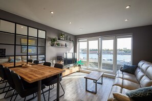 Una sala de estar moderna con comedor, sofá, televisor y vista al agua.