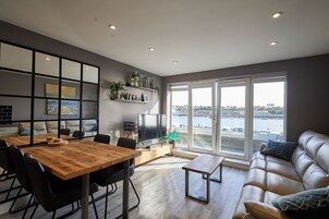 Una sala de estar moderna con comedor, sofá, televisor y vista al agua.