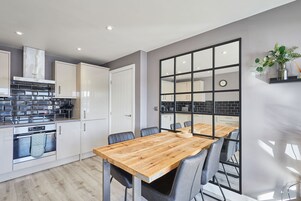 A modern kitchen with white cabinets, a wooden dining table, and a view into the adjacent dining area.