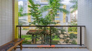 A balcony with a view of a residential area, a wooden bench, and a tiled floor. - Apartamento em Ubatuba a 50m da Praia Grande (Ubatuba)