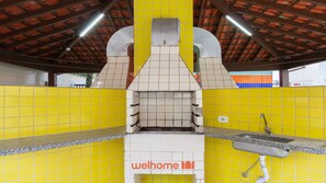 A kitchen with a pizza oven, yellow tiled walls, and a welcome sign. - Apartamento em Ubatuba a 50m da Praia Grande (Ubatuba)