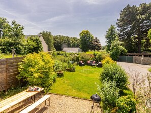 Un jardin avec un barbecue, un coin salon et une table en bois sur laquelle se trouve un plateau rempli de divers objets.