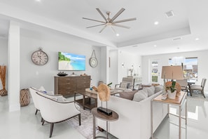 A spacious living room with a large flat-screen TV, a ceiling fan, and a view of the outdoors through a large window. - Perfect 4-bedroom house with AC in charming Naples (Naples)