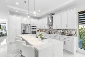 A modern kitchen with white cabinetry, a marble countertop, and a large island with bar stools. - Perfect 4-bedroom house with AC in charming Naples (Naples)