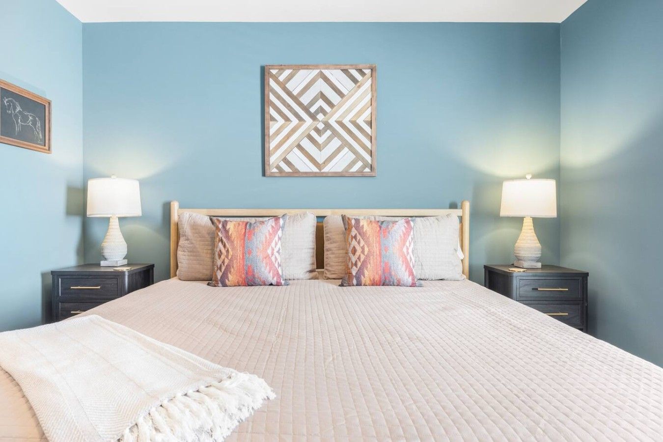 A bedroom with a bed, two bedside tables, a headboard, and a wall-mounted decorative piece.