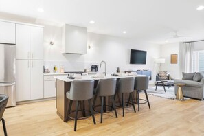 A modern kitchen with a central island, bar stools, and a dining area with a sofa and coffee table. - Rooftop Deck with BBQ & TV, 3 Miles to Downtown, Garage (Nashville)