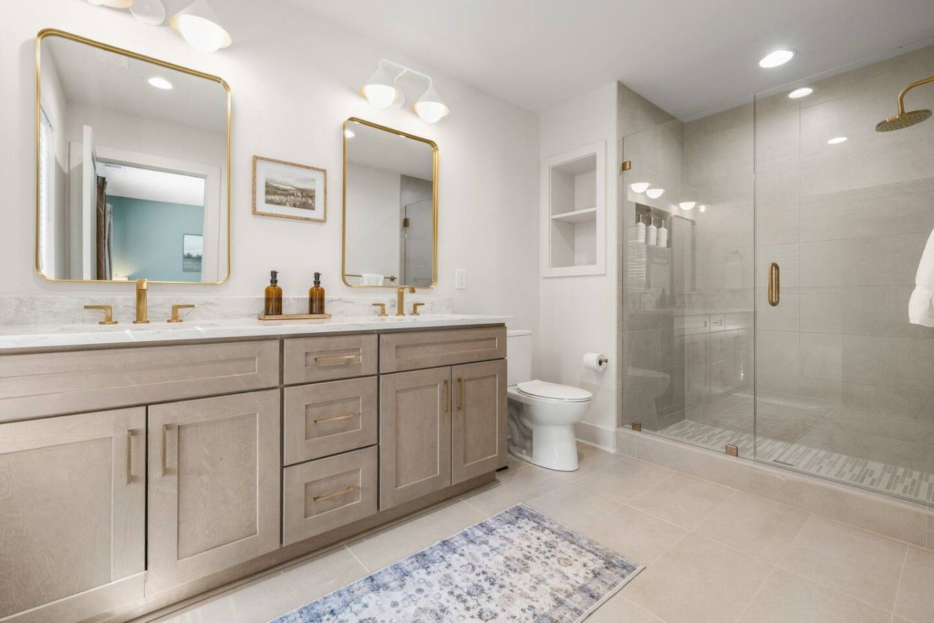 A bathroom with a double vanity, a toilet, a shower enclosure, and a patterned rug.