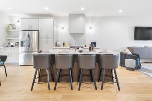 A modern kitchen with a central island, bar stools, and a flat-screen TV. - Rooftop Deck with BBQ & TV, 3 Miles to Downtown, Garage (Nashville)