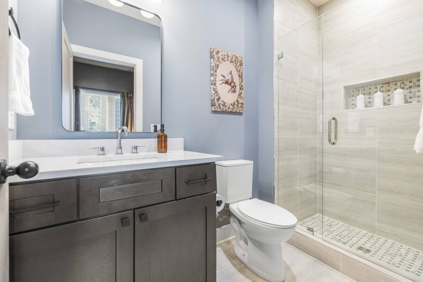 A bathroom with a white sink, dark cabinets, a toilet, and a glass shower enclosure.