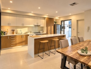 Een moderne keuken met een centraal eiland, barkrukken en een eettafel met stoelen.