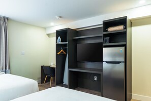 A hotel room with a bed, a desk, a chair, a wardrobe, and a refrigerator.