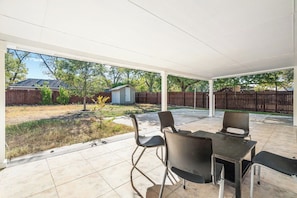 A covered patio with a table and chairs, a wooden fence, and a small shed in the background. - Spacious 3BR w/ Fenced Yard, Near Austin Downtown (Austin)