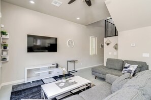 Un salon moderne avec un téléviseur à écran plat, un canapé gris, une console blanche et un escalier doté d’une rampe noire.