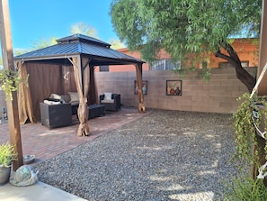 A covered outdoor seating area with a pergola, a brick patio, and decorative wall art. - Gather & Unwind | Patio | Ramada, BBQ | 3BR (Tucson)