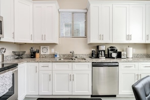 A kitchen with white cabinets, a granite countertop, a dishwasher, a coffee maker, and a toaster. - Gather & Unwind | Patio | Ramada, BBQ | 3BR (Tucson)