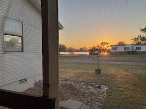 A view through a window with a mesh screen, displaying a sunset and a distant building.