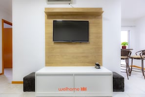 Une chambre moderne avec un téléviseur à écran plat fixé à un mur en bois, une console blanche ornée d’un logo et des meubles en osier.
