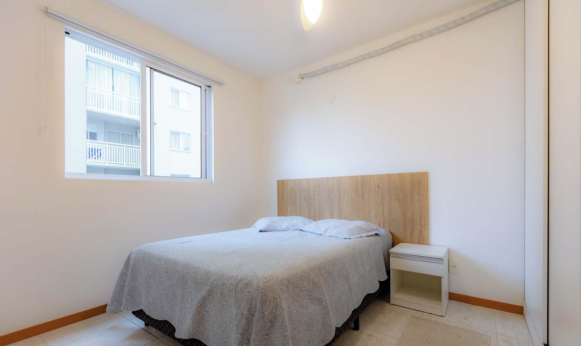 A bedroom with a bed, a nightstand, a window, and a view of a balcony.