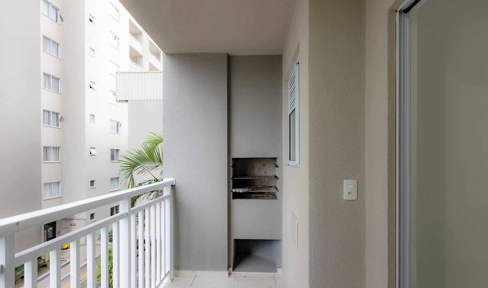 Ein schmaler Balkon mit weißer Brüstung, einer kleinen Pflanze und Blick auf ein mehrgeschossiges Gebäude.